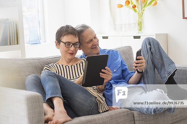 Senior couple sharing electronic devices on sofa