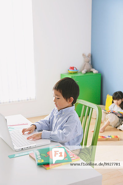 Elementary age boy doing his homework at his desk with his sister reading on the floor in the background