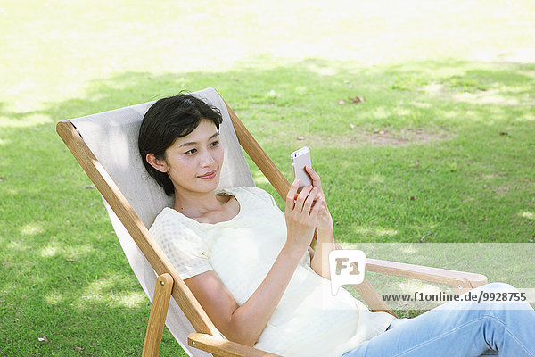Japanese woman with smartphone on deck chair in a city park