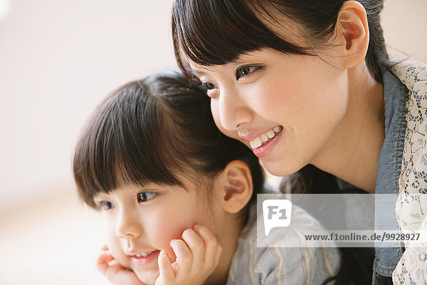 Young adult mother and daughter smiling while looking away