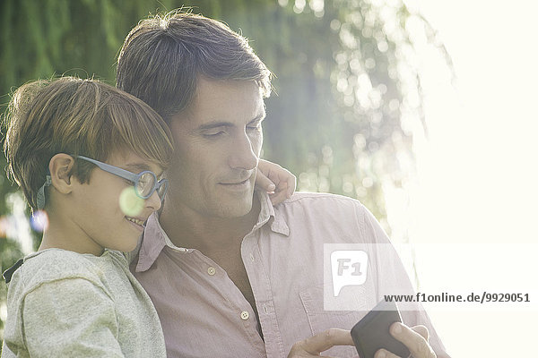 Vater und Sohn betrachten Smartphone im Freien  Überbelichtung