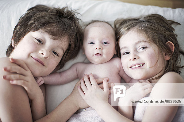 Junge und Mädchen liegen auf dem Bett mit dem kleinen Bruder  Portrait