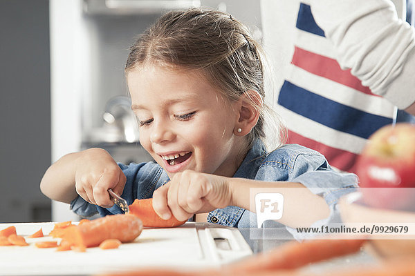 Little girl slicing carrots in kitchen