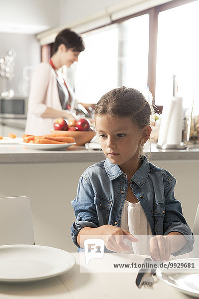 Mädchen beim Tischdecken  Mutter beim Essen im Hintergrund