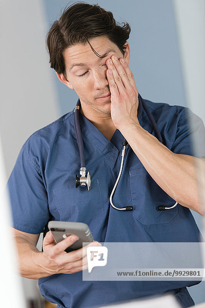 Tired Hispanic doctor holding cell phone in hospital