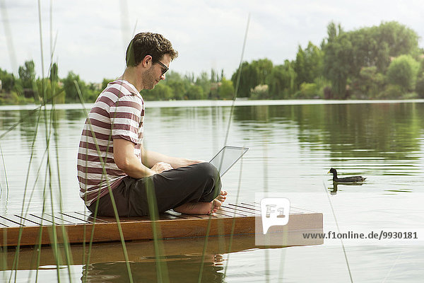 Man sitting on dock using laptop computer