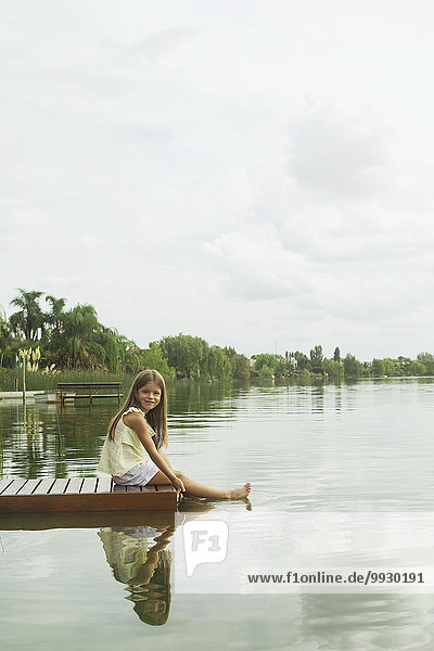 Mädchen auf Dock sitzend mit im See baumelnden Füßen  Portrait