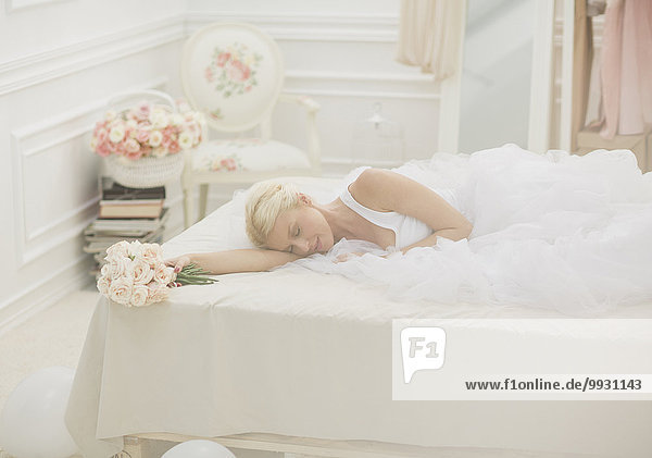 Bride sleeping on bed with bouquet of flowers
