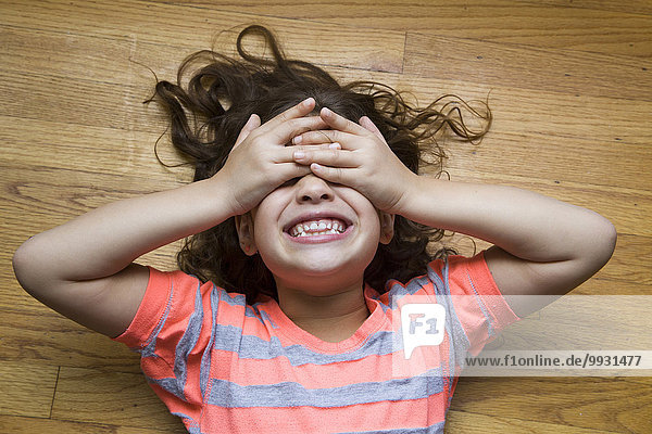 Smiling Hispanic girl covering her eyes on floor
