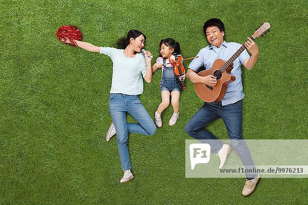 A family of three lying on the grass with a musical instrument