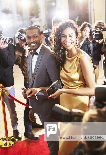 Smiling celebrity couple being photographed by paparazzi photographers at red carpet event