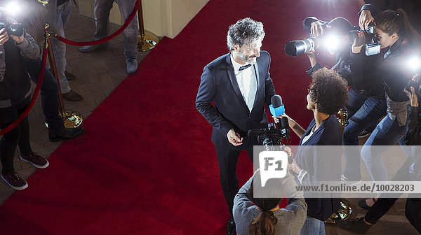 Celebrity being interviewed and photographed by paparazzi photographers at red carpet event