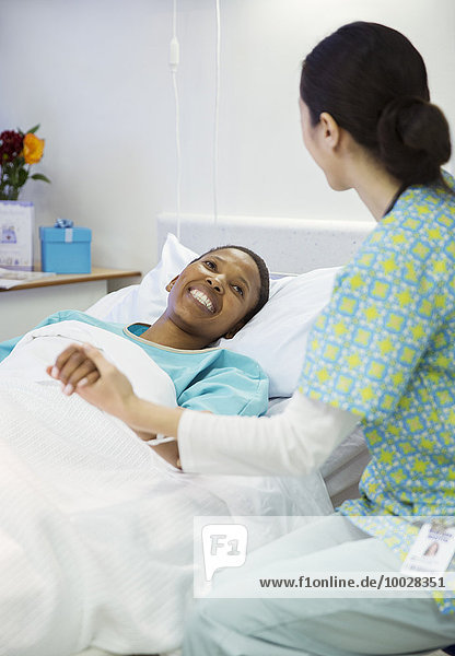 Nurse holding smiling patient’s hand in hospital room