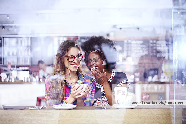 Frauen lachen und trinken Kaffee im Caféfenster