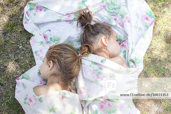 Twin girls napping in floral sheet on grass
