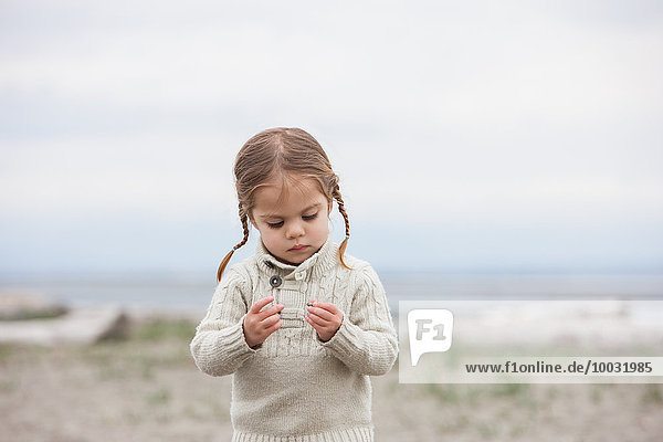 Neugieriges Mädchen untersucht Kieselsteine am Strand