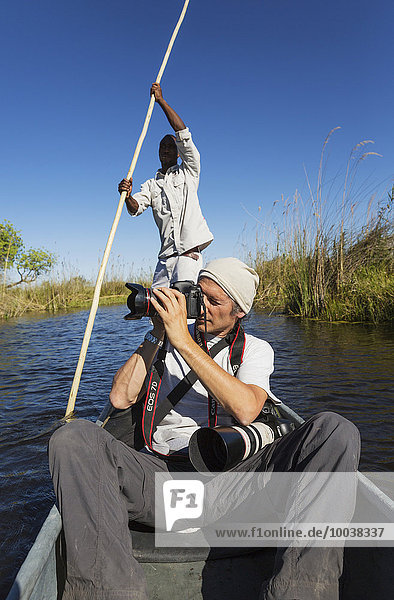 Game viewing safari  photographer in a traditional Mokoro boat  Okavango Delta  Moremi Game Reserve  Botswana  Africa