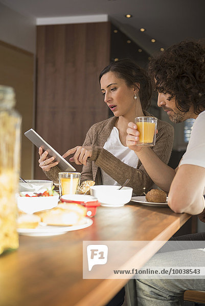 Mid adult woman using a digital tablet with her husband over breakfast  Munich  Bavaria  Germany