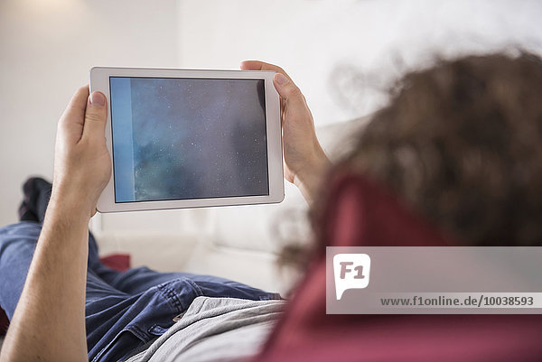 Man lying down on couch and using a digital tablet  Munich  Bavaria  Germany