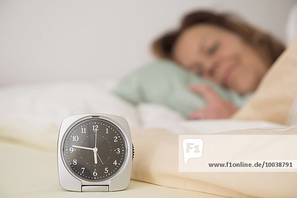 Woman asleep in bed while her alarm shows the early time at home in bedroom  Munich  Bavaria  Germany