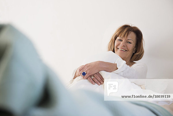 Portrait of senior woman sitting on bed and smiling  Munich  Bavaria  Germany