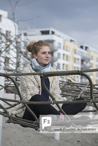 Young woman sitting on climbing net in playground  Munich  Bavaria  Germany