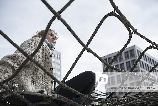 Low angle view of a young woman sitting on climbing net  Munich  Bavaria  Germany