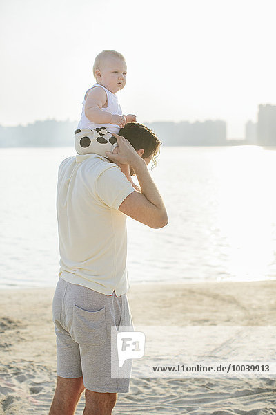 father carrying baby on shoulders at beach