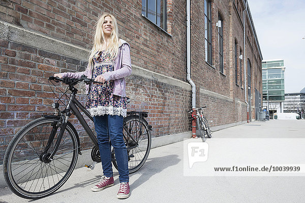 Teenage girl with bicycle against brick wall  Munich  Bavaria  Germany