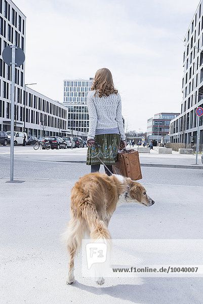 Rear view of woman walking on road with dog and suitcase  Munich  Bavaria  Germany