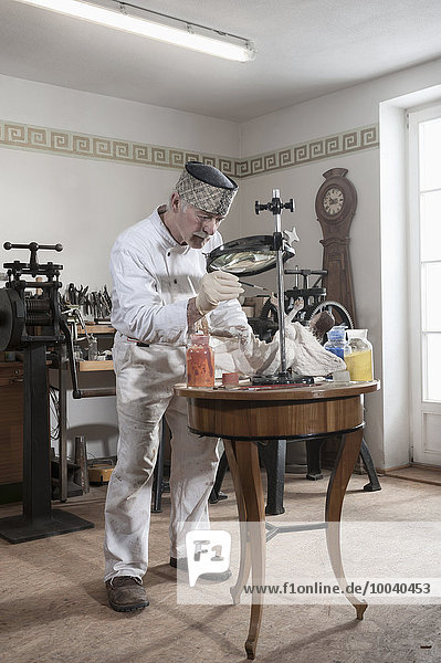 Senior sculptor colouring a Jesus Christ statue at workshop  Bavaria  Germany