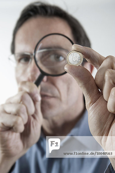 Businessman examining one euro coin with magnifying glass  Bavaria  Germany