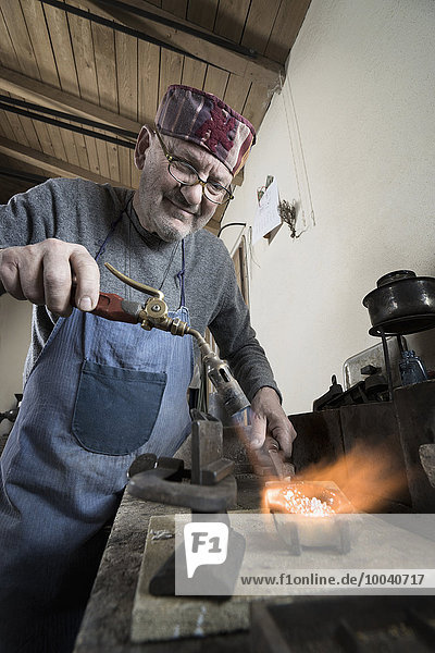 Senior male jeweler melting and casting with blow torch at workshop  Bavaria  Germany