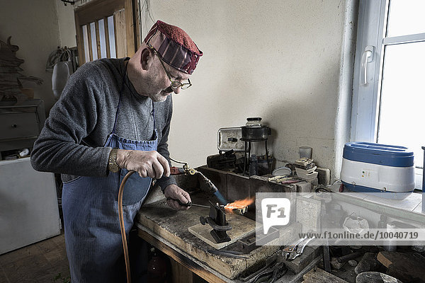 Senior male goldsmith melting and casting with blow torch at workshop  Bavaria  Germany
