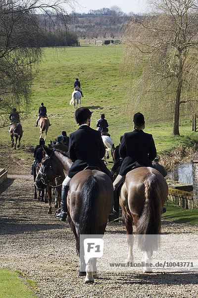 A foxhunt in progress  riders on horseback wearing hard hats riding across countryside.