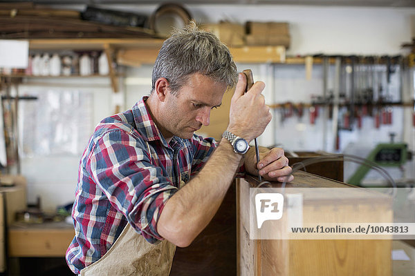 An antique furniture restorer using a handheld work tool and working on the polished top of a piece of furniture.