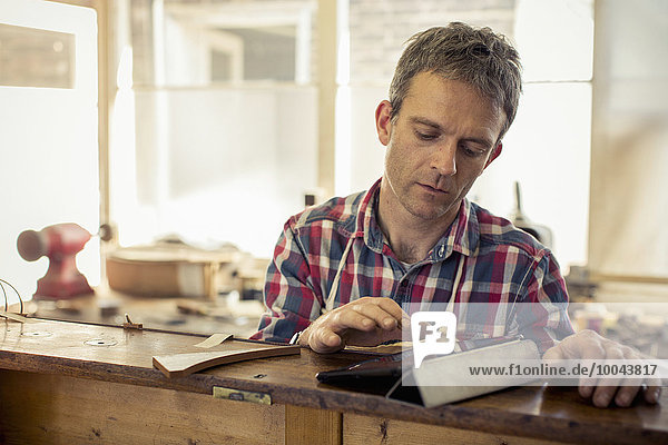 An antique furniture restorer  a craftsman using a digital tablet in the course of his work.