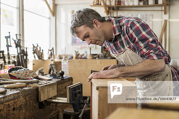 An antique furniture restorer in his workshop using a hand tool to smooth a wooden object.