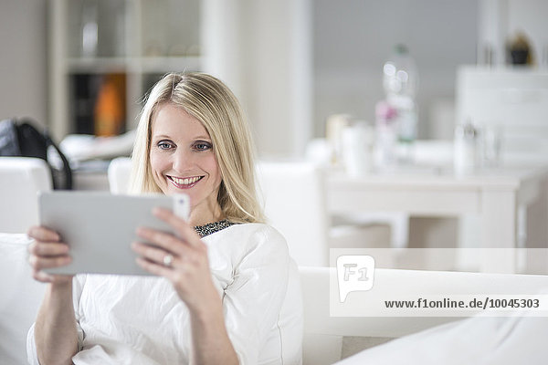 Porträt einer lächelnden blonden Frau mit Mini-Tablette zu Hause