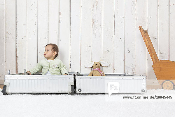 Kleines Mädchen sitzend im offenen Koffer mit Plüschtier,  wegschauend