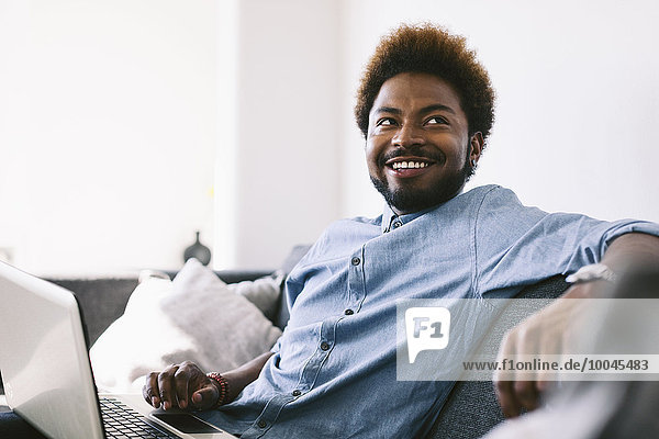 Young Afro American man sitting on couch  using laptop