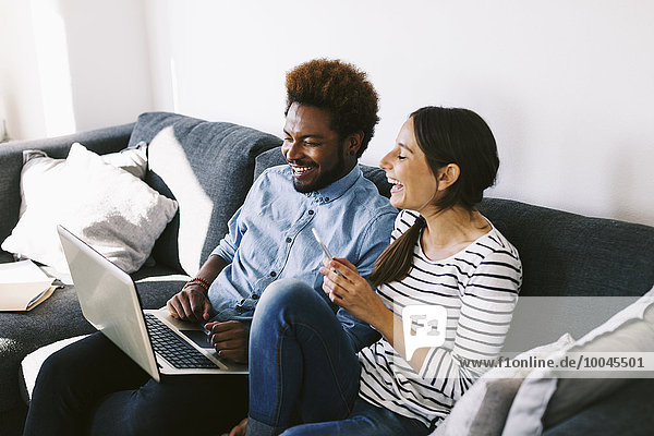 Young couple sitting on couch  using laptop and smart phone