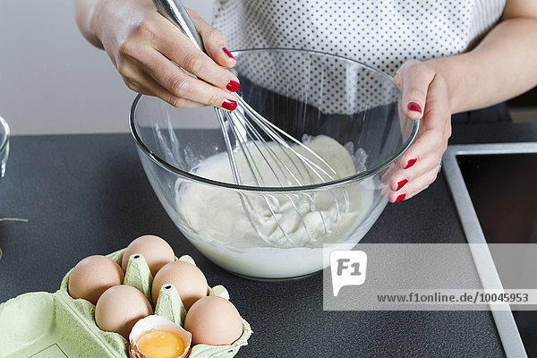Woman stirring dough in a glassbowl with wire whisk