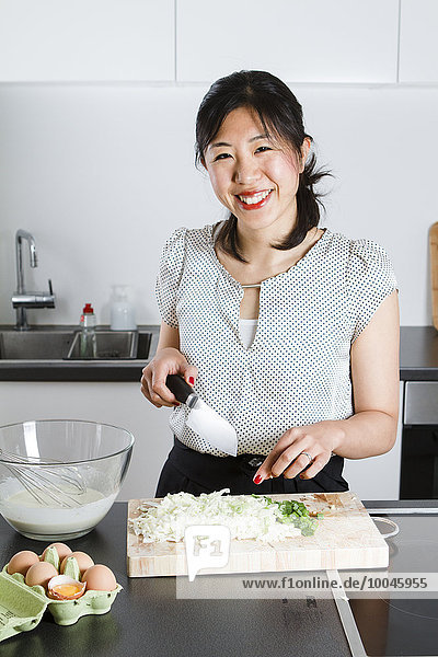 Porträt einer lächelnden Frau beim Schneiden von Frühlingszwiebeln in der Küche