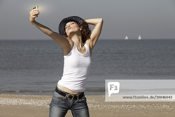 Niederlande  Scheveningen  junge Frau mit einem Selfie am Strand