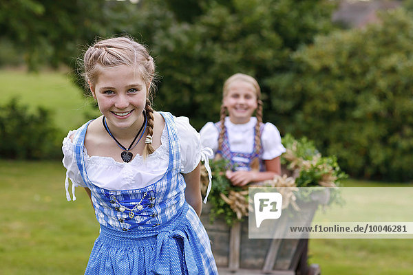 Deutschland  Lüneburger Heide  Porträt eines lächelnden blonden Mädchens im Dirndl  das den Erntewagen zieht
