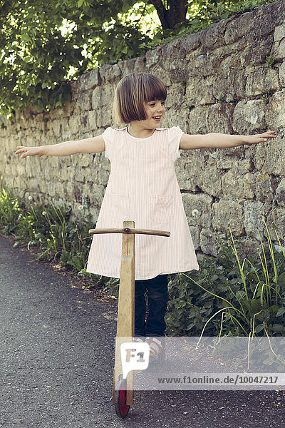 Kleines Mädchen  das auf einem alten Holzroller balanciert.