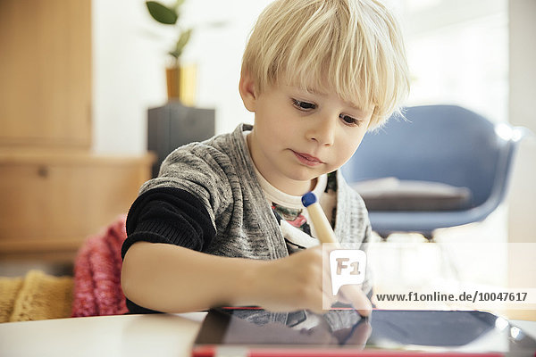 Porträt eines kleinen Jungen mit einem digitalen Stift auf einem digitalen Tablett zu Hause