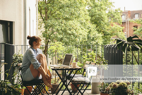 Smiling woman looking at her laptop on balcony