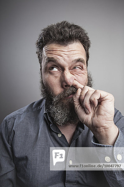 Portait of a mature man with full beard  picking his nose